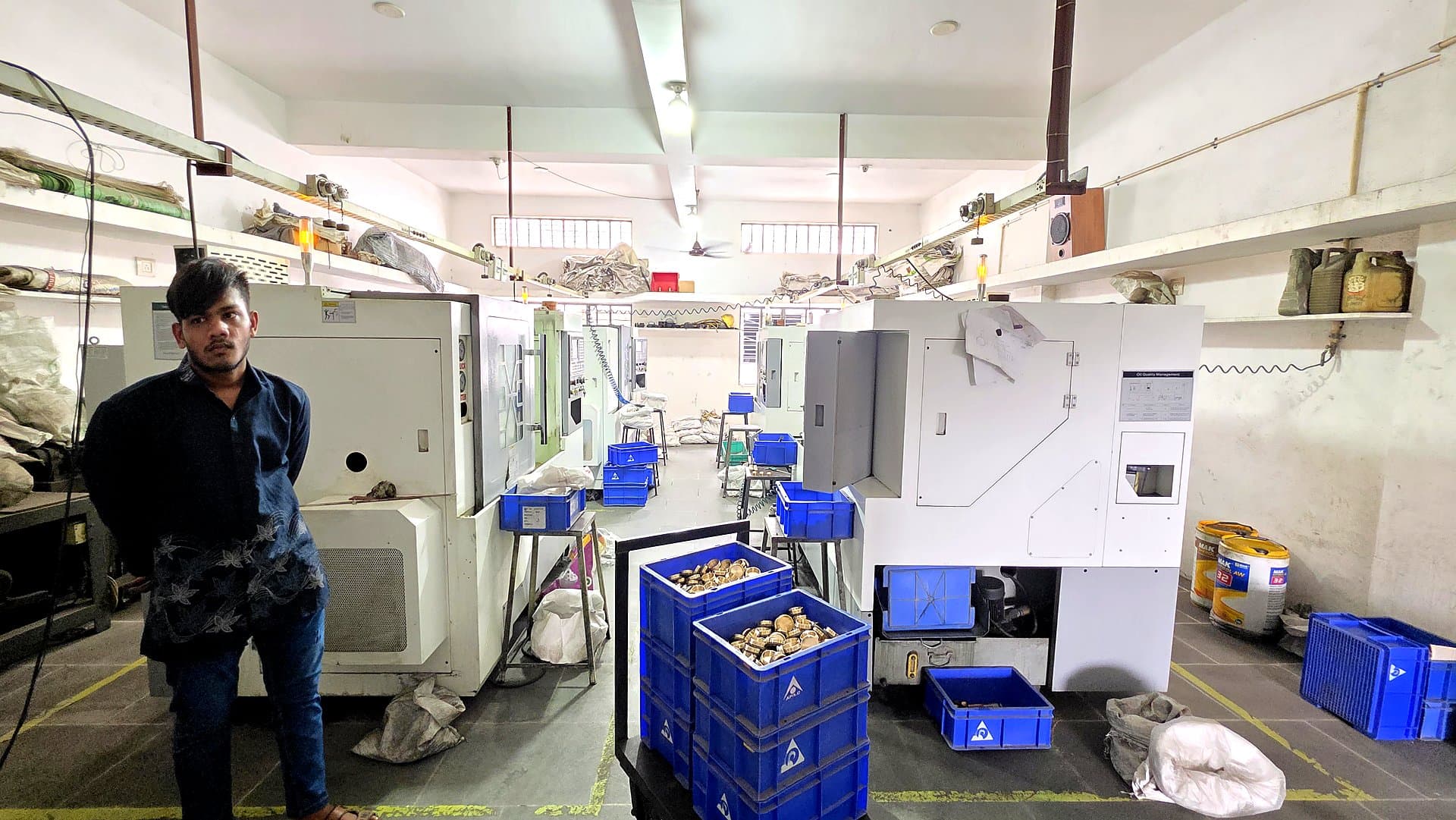 Worker operating CNC machine with brass parts in blue crates